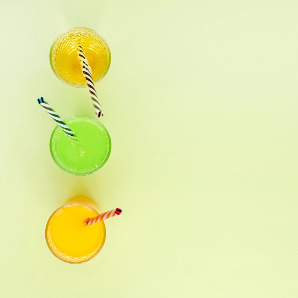 Three fresh juices in clear bottles/cups arranged as a trio on a clean, modern background